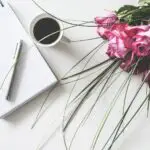 Red Rose Flowers Bouquet on White Surface Beside Spring Book With Click Pen and Cup of Cofffee